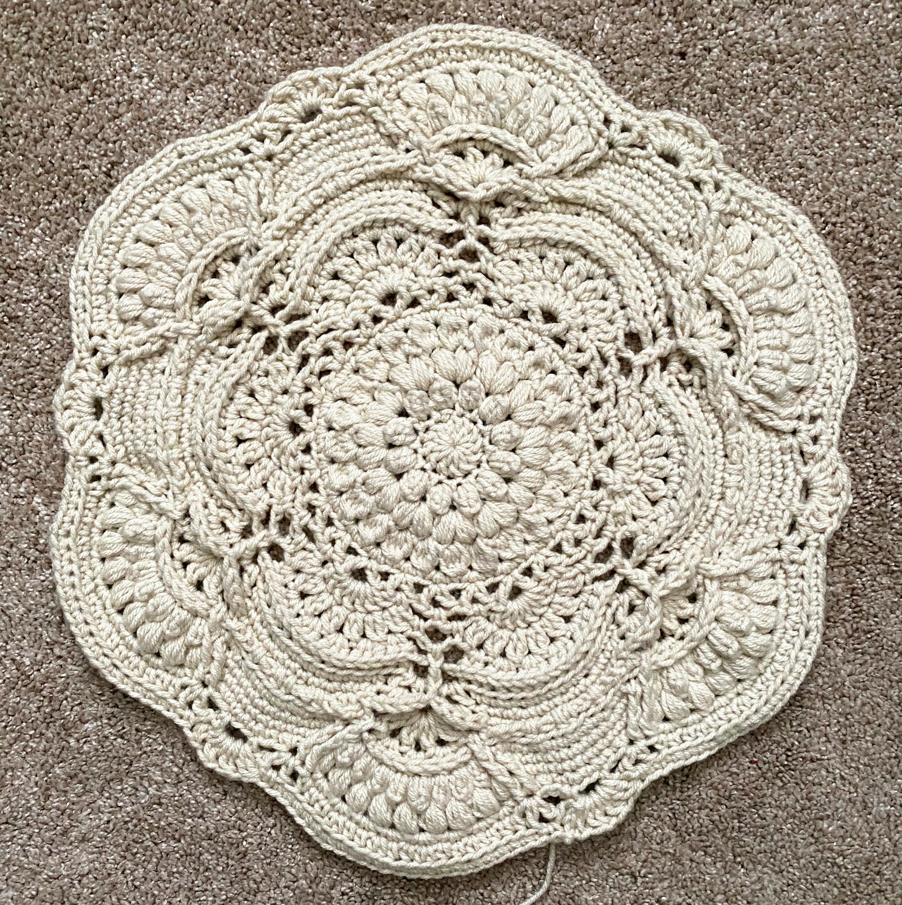 Beginning stages of a off-white crochet circle-shaped blanket with textured stitches.